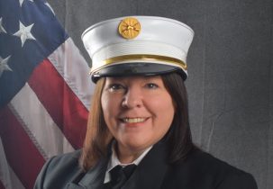 Photo of Jennifer Bossi in Class A uniform in front of draped American Flag