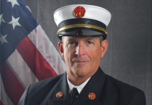 Portrait of Steve Lennon in a Class A uniform in front of an American flag backdrop